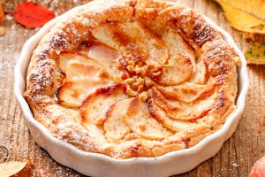 Apple tart with the addition of cinnamon sprinkled with powdered sugar on a wooden table. A delicious homemade dessert